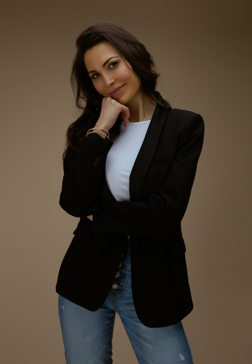 Bella French wears a black blazer, white t-shirt and blue jeans and tilts her head and smiles at the camera.