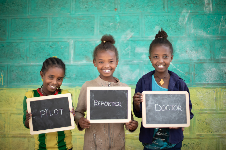 Children holding up small chalkboards with words pilot, reporter, and doctor written on them
