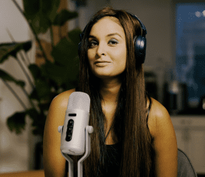 A photo of Fatima Zaidi in front of a podcast microphone smiling at the camera to showcase her as the author of this article about philanthropic podcasts