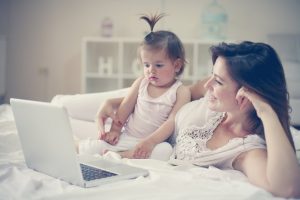 A mom and baby look at a laptop while lying on a bed.
