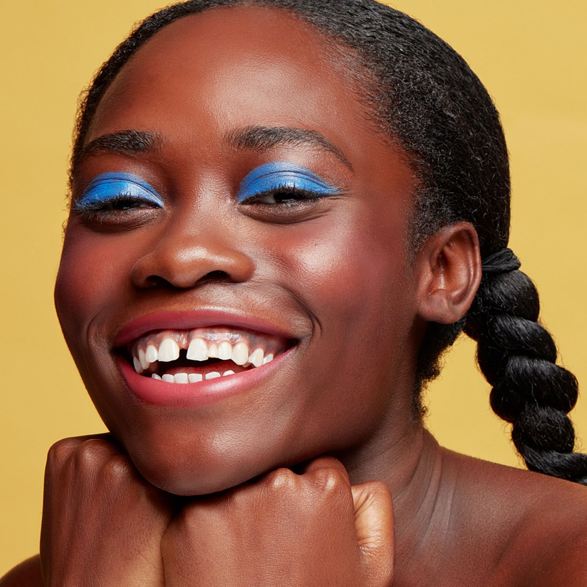 A woman with bright blue eyeshadow smiling at the camera, showcasing some makeup from bipoc beauty brand, Cheekbone Beauty