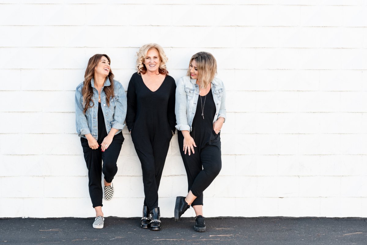 Mercedes LaPorte(L), Teresa Freeborn(C), and Ashley Freeborn(R) of Smash + Tess stand together laughing and smiling against a wall outside.