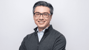 BGC Canada CEO Owen Charters smiling in a half-zip grey sweater and glasses against a grey background.