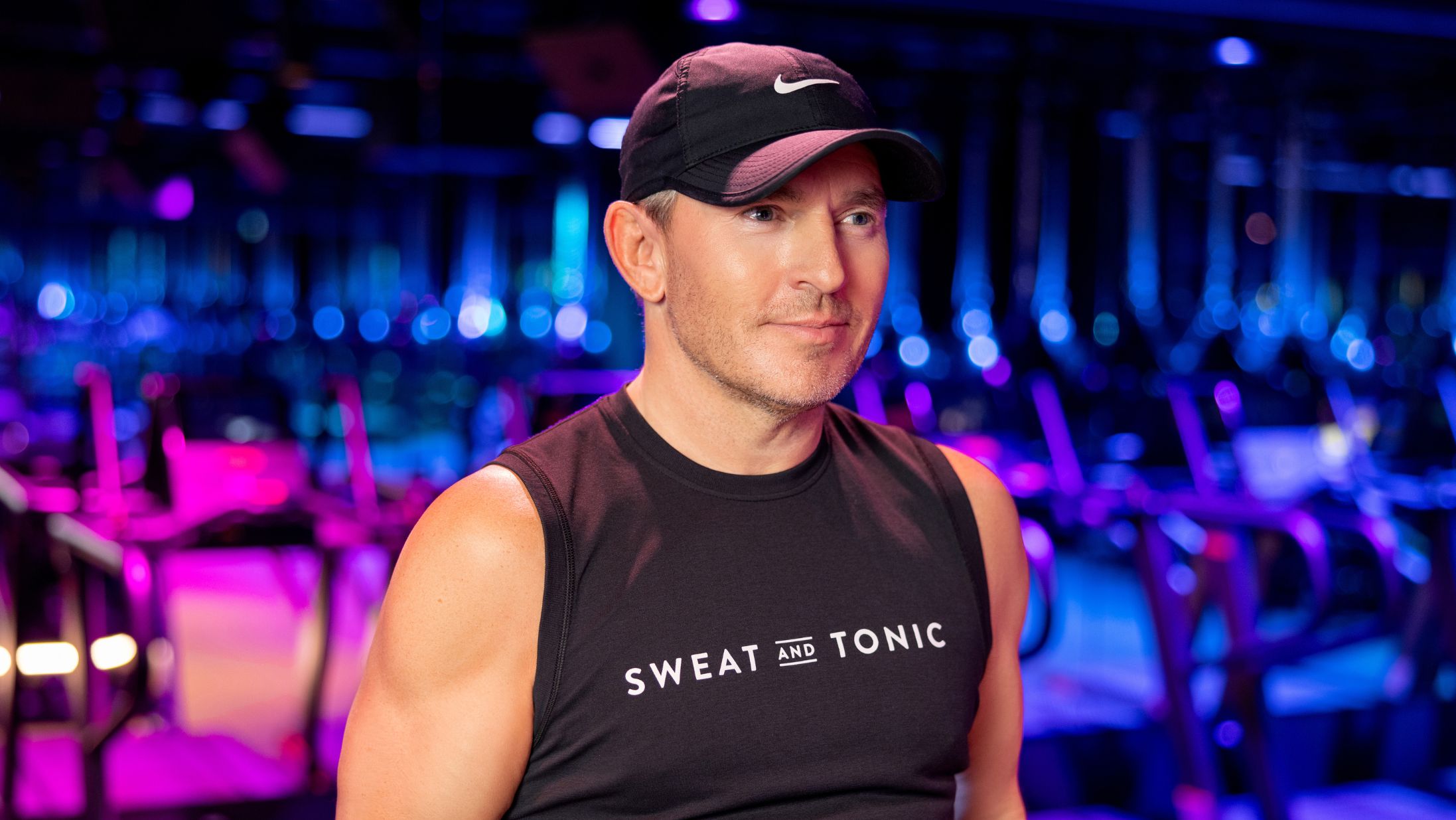David Ingram wearing a sleeveless branded Sweat and Tonic shit and baseball hat in a gym.