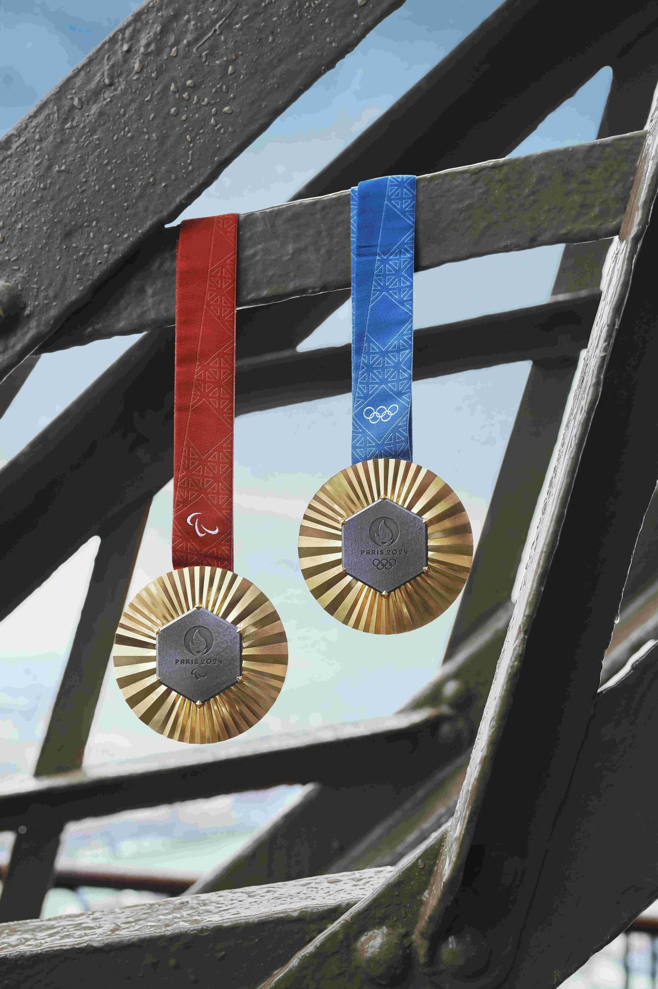 An Olympic medal with blue satin ribbon and paralympic medal with red satin ribbon hanging off the edge of the eiffel tower.