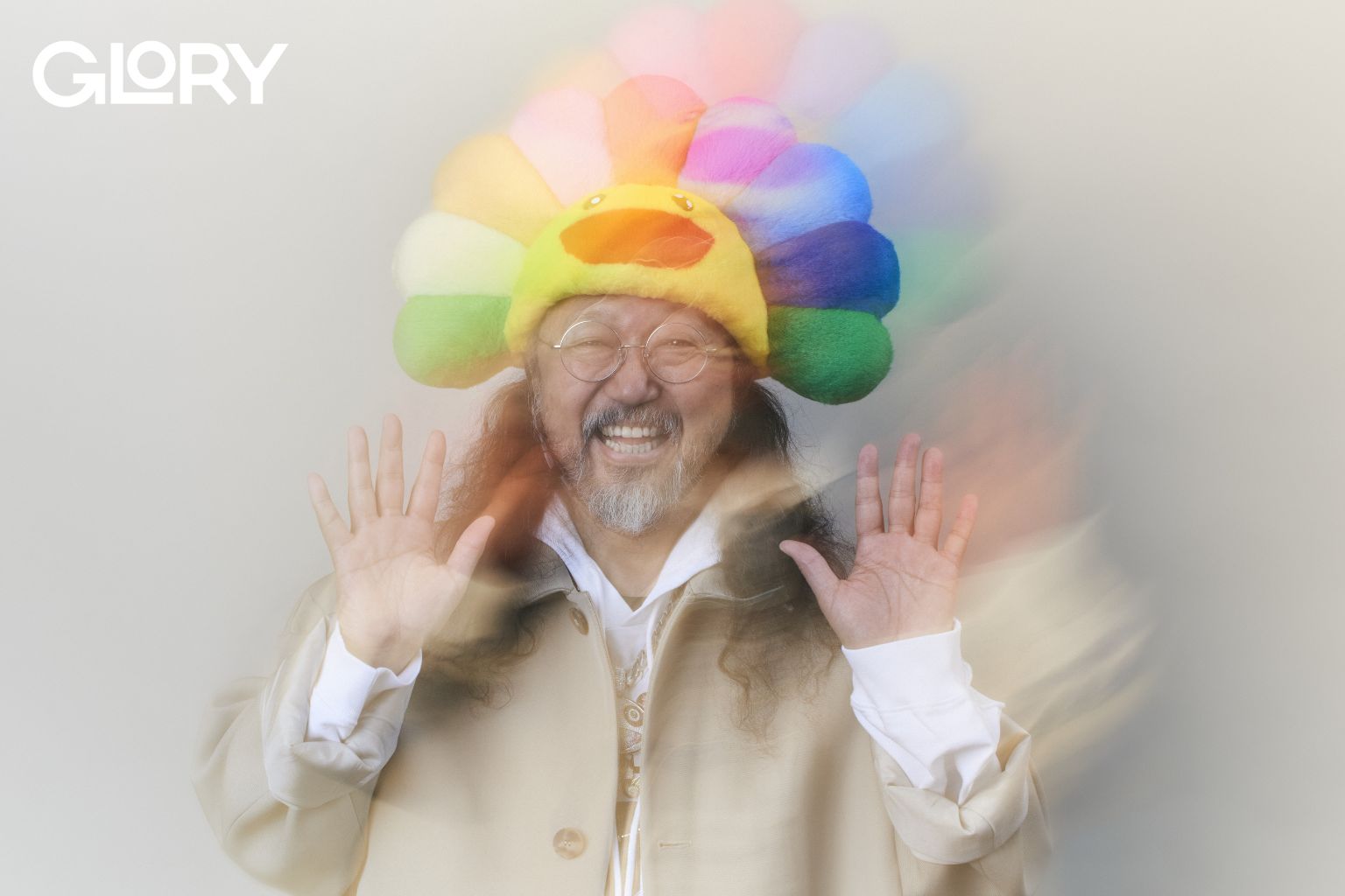 Takashi Murakami wearing a rainbow hat and smiling into the camera with a blurred effect.