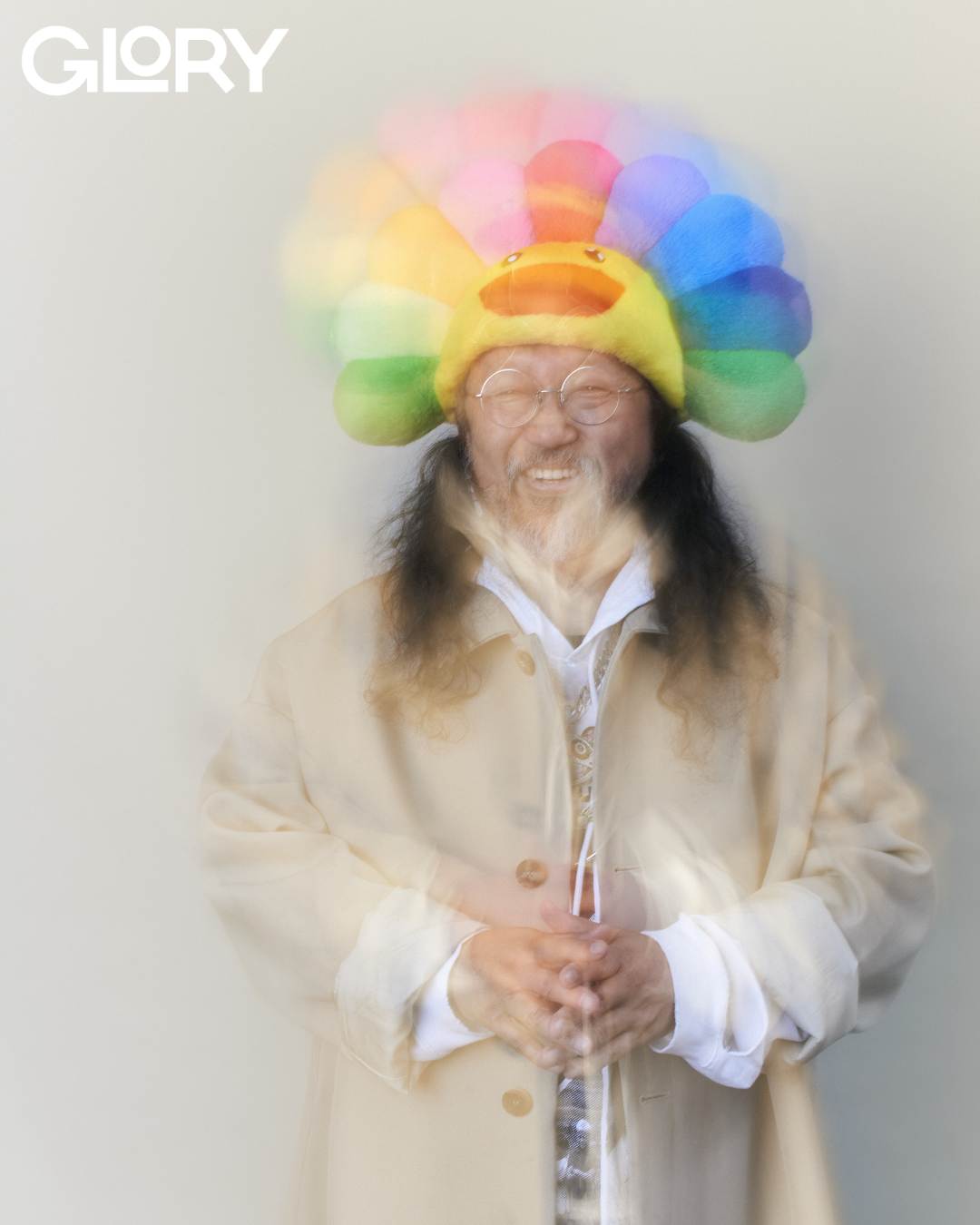 Takashi Murakami wearing a rainbow hat and smiling into the camera with a blurred effect.