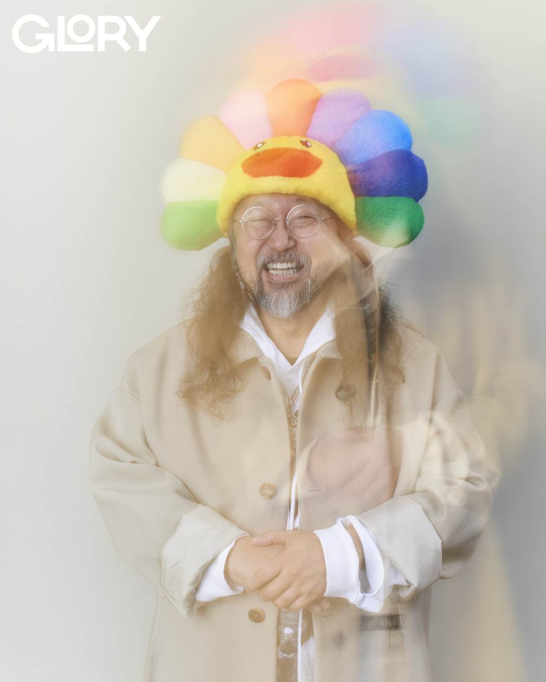 Takashi Murakami wearing a rainbow hat and smiling into the camera with a blurred effect.