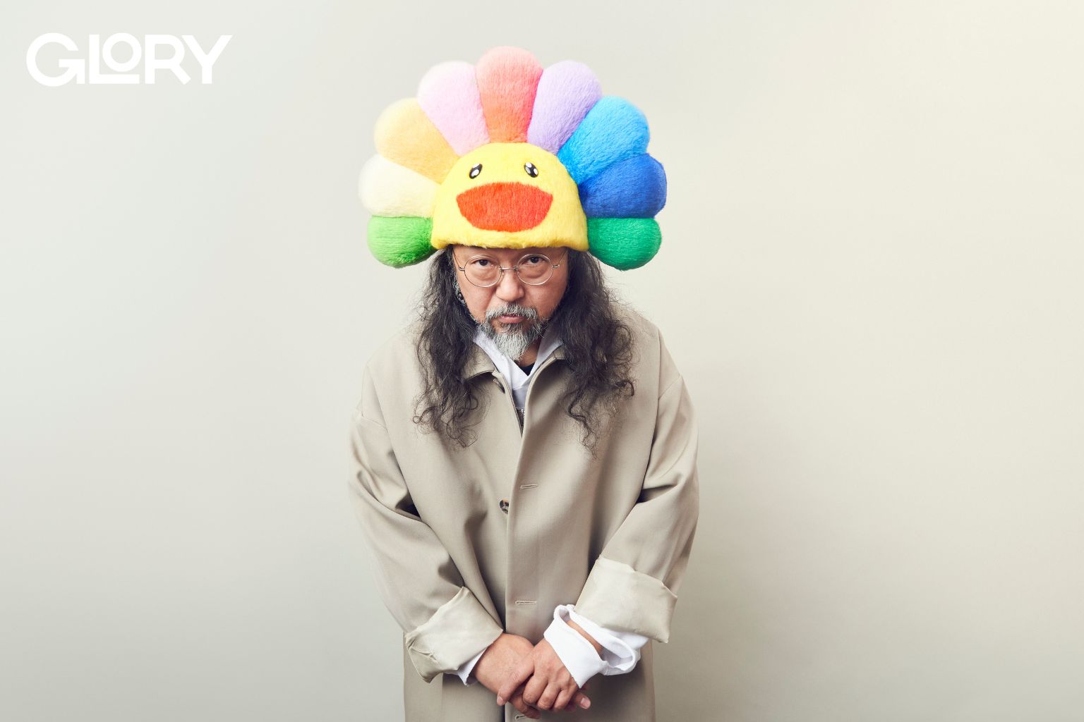 Takashi Murakami wearing a rainbow hat. He is looking at the camera and bowing.