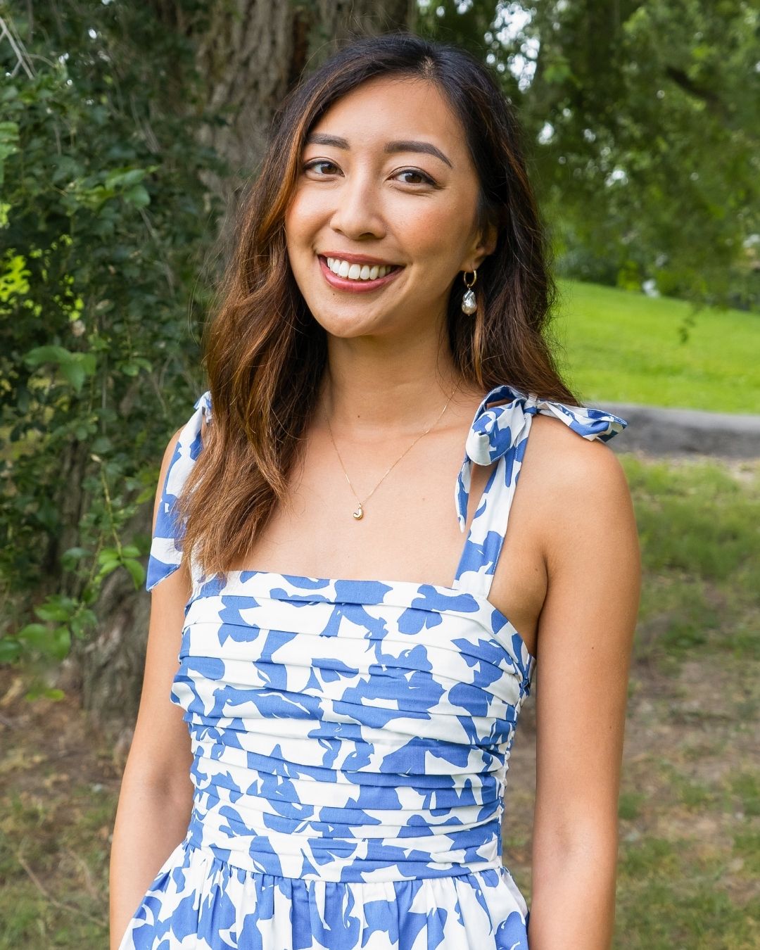 Connie Lo wearing a blue and white floral dress against the backdrop of a park.