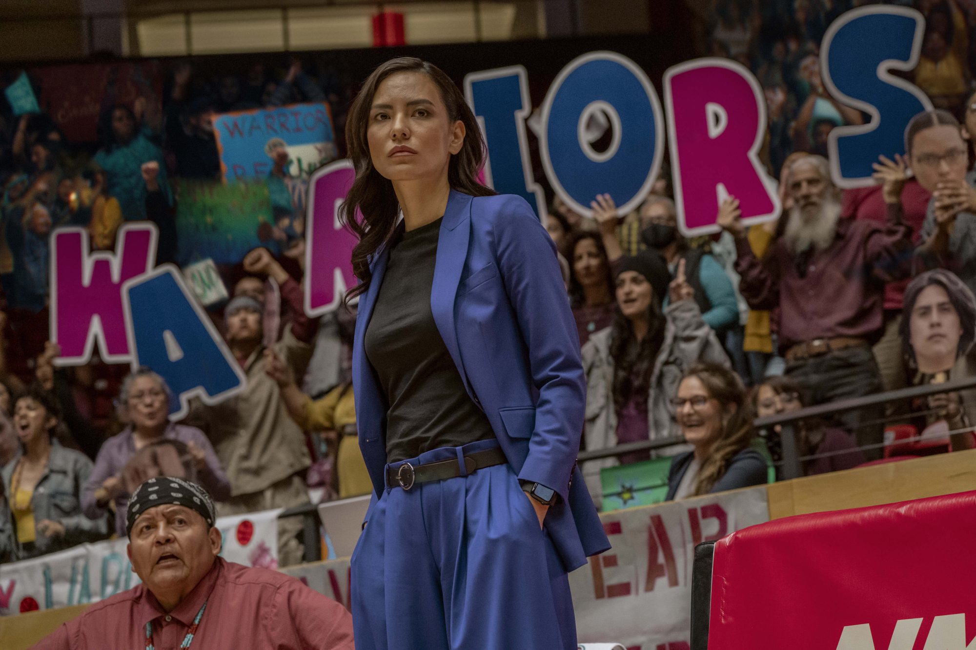 Jessica Matten in a blue suit against a crowd at a basketball game