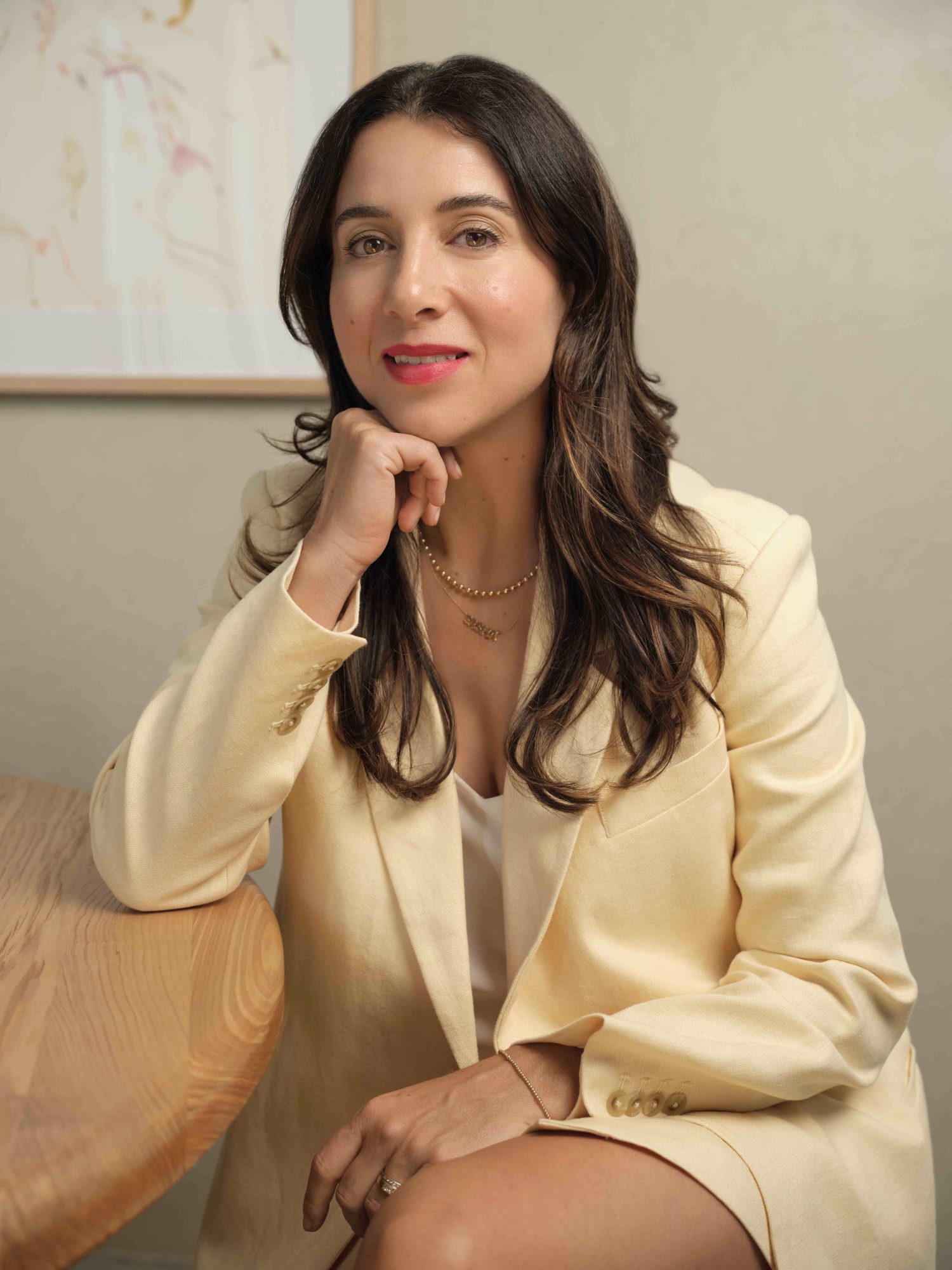 Sasha Plavsic leaning against a table wearing a white blazer.